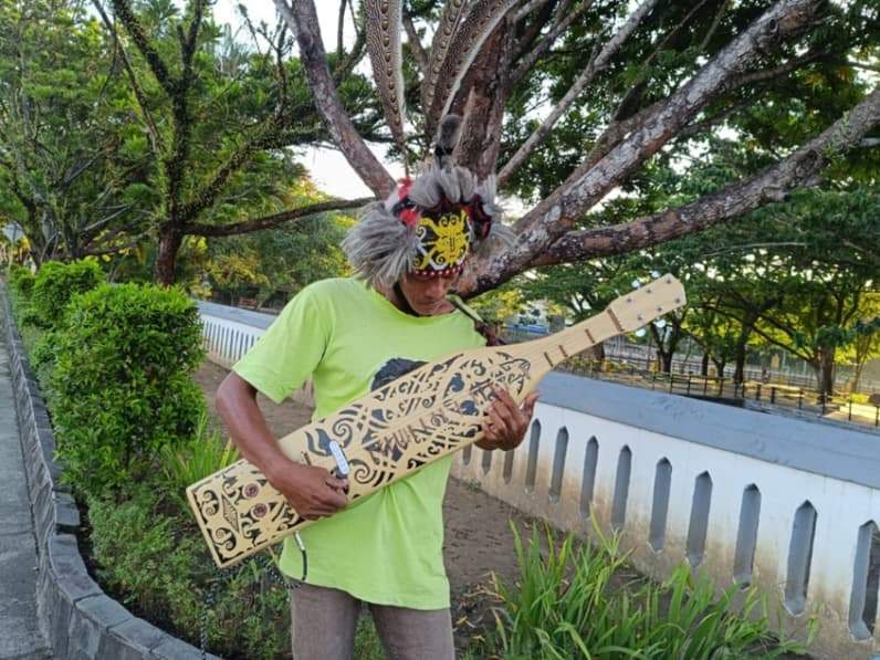 Agus Leo Saputra memainkan alat musik Sape di simpang Bendali Telaga Sari Balikpapan, Sabtu (18/7/2026). (Foto: Achmad Fadillah/Pusaranmedia.com)